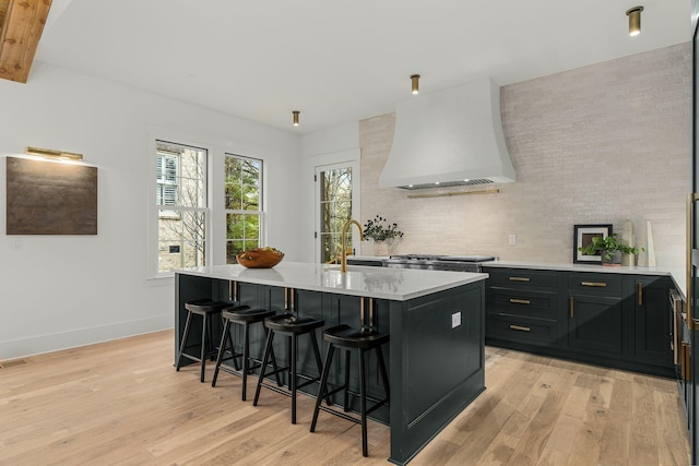 kitchen featuring premium range hood, sink, a center island with sink, light hardwood / wood-style flooring, and a breakfast bar area