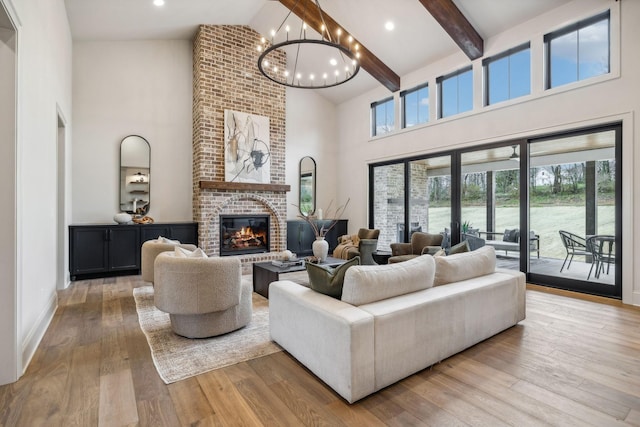 living room featuring a brick fireplace, beam ceiling, an inviting chandelier, light hardwood / wood-style flooring, and high vaulted ceiling