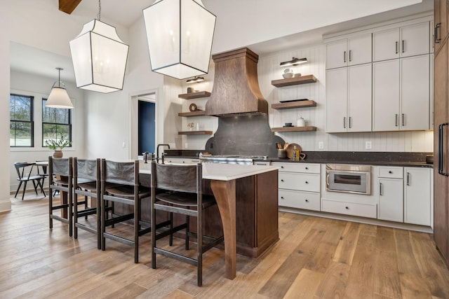 kitchen featuring a center island with sink, decorative light fixtures, light hardwood / wood-style floors, and white cabinetry