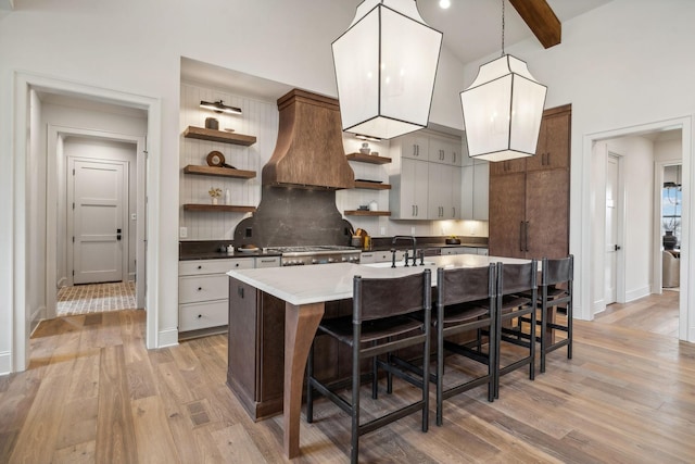 kitchen with sink, a kitchen bar, a center island with sink, stainless steel stove, and light wood-type flooring