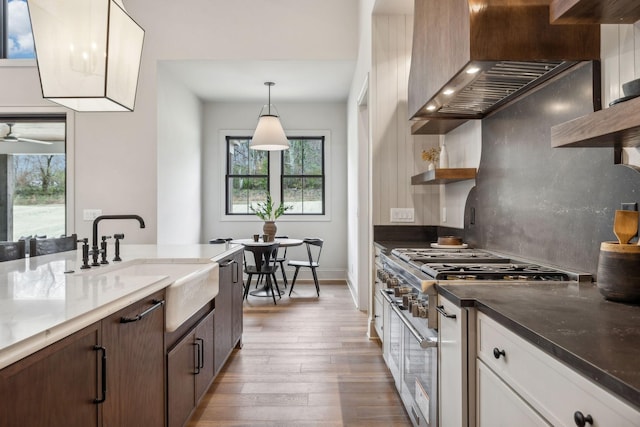 kitchen with wall chimney range hood, sink, pendant lighting, white cabinets, and dark hardwood / wood-style floors