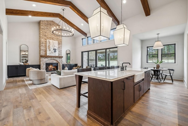 kitchen featuring a kitchen island with sink, sink, light wood-type flooring, decorative light fixtures, and beam ceiling