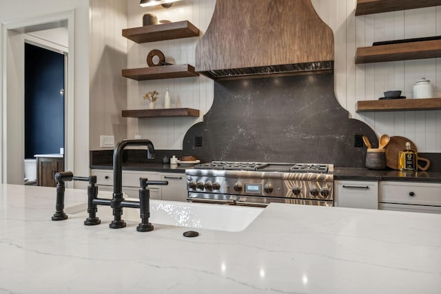 kitchen featuring high end stove, backsplash, light stone counters, and custom exhaust hood