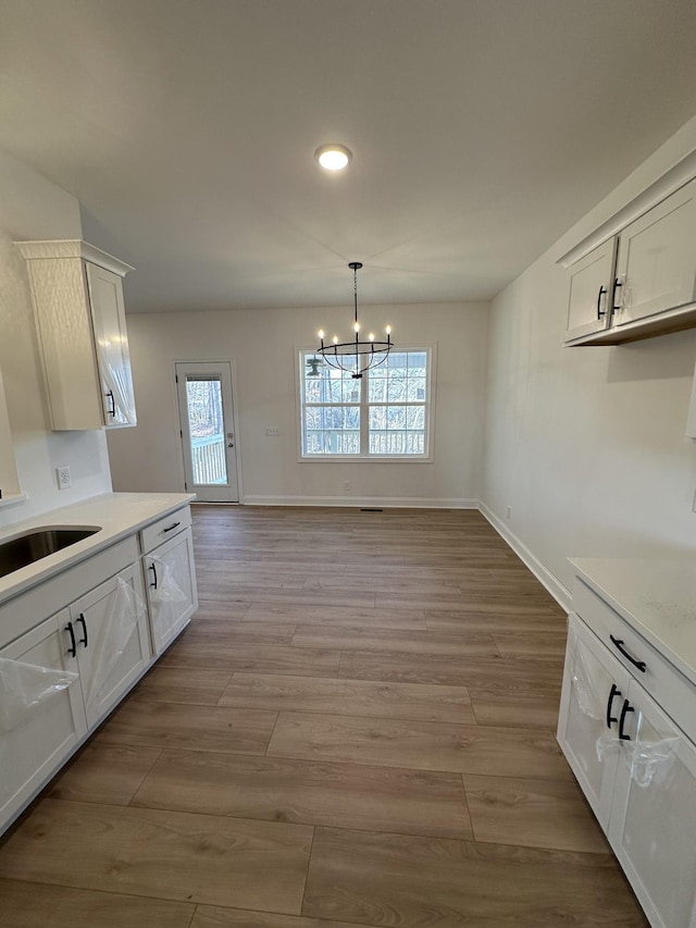 unfurnished dining area featuring sink, a healthy amount of sunlight, an inviting chandelier, and light wood-type flooring