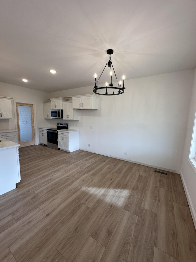 unfurnished dining area with pendant lighting, hardwood / wood-style floors, a chandelier, and white cabinets