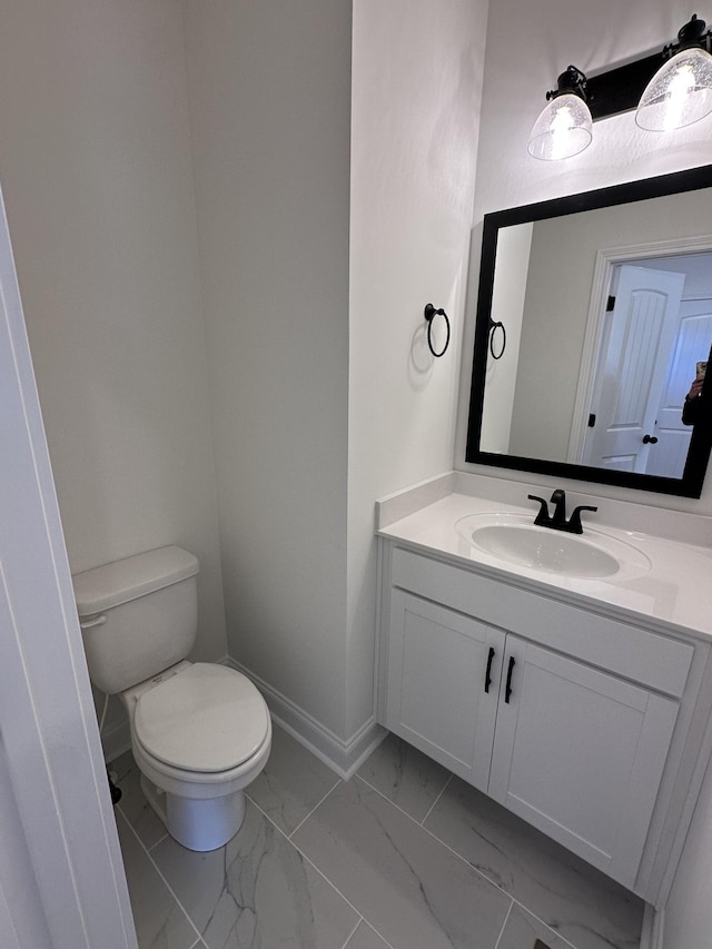 half bath with baseboards, marble finish floor, toilet, and vanity