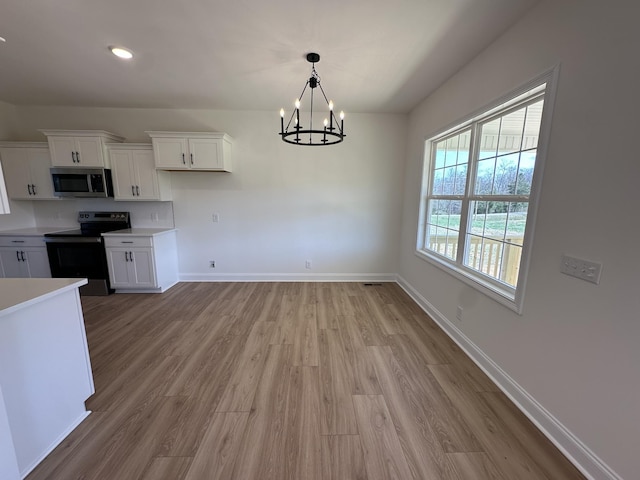 kitchen featuring baseboards, stainless steel microwave, white cabinets, and black / electric stove