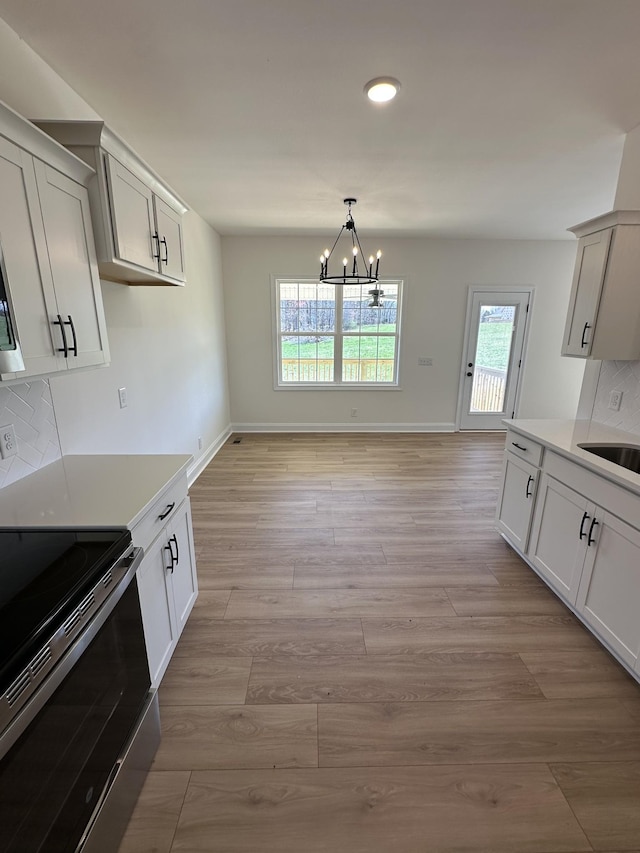 kitchen with electric range, a notable chandelier, backsplash, and light wood-type flooring