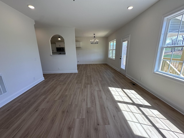 unfurnished living room with an inviting chandelier, dark wood-style floors, baseboards, and recessed lighting