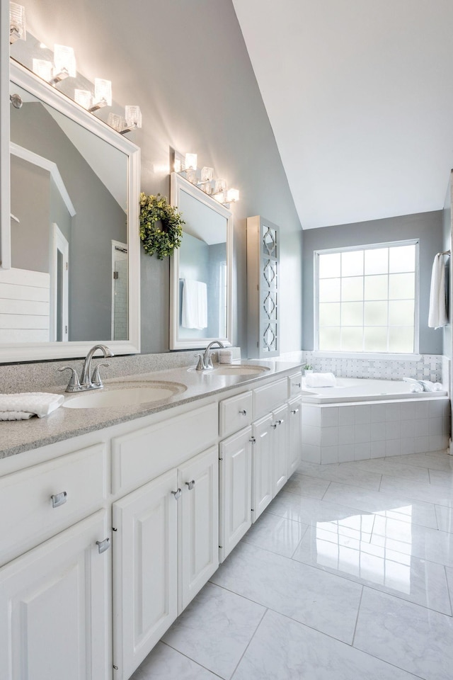 bathroom with vanity, a relaxing tiled tub, and vaulted ceiling