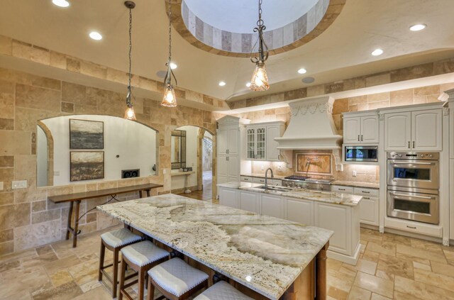 kitchen with decorative light fixtures, a spacious island, custom exhaust hood, sink, and appliances with stainless steel finishes