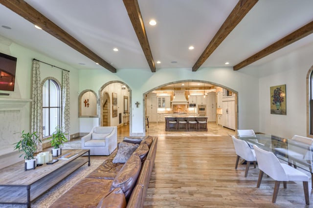 living area featuring arched walkways, beamed ceiling, recessed lighting, and light wood-style floors