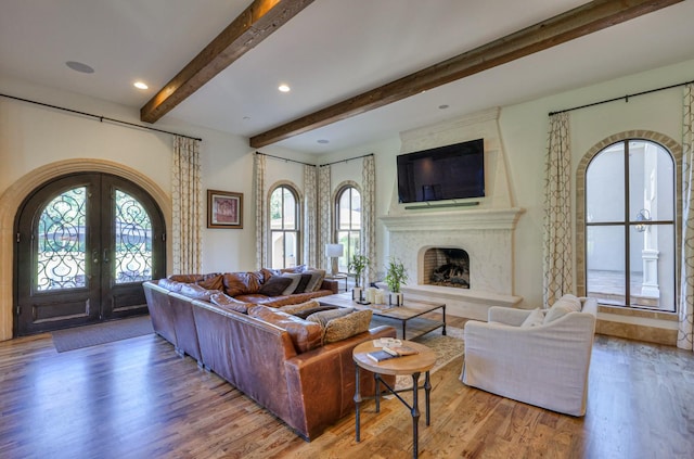 living area with arched walkways, a premium fireplace, beamed ceiling, wood finished floors, and french doors