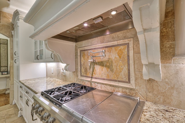 kitchen featuring light stone countertops, light tile flooring, premium range hood, backsplash, and white cabinetry