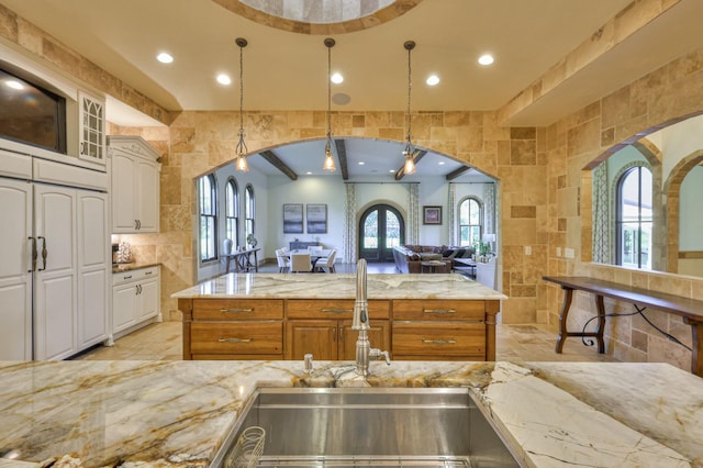 kitchen with arched walkways, light stone counters, open floor plan, a healthy amount of sunlight, and tile walls