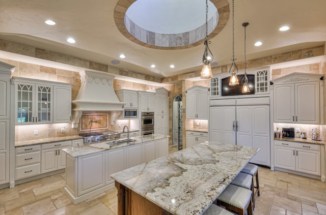 kitchen with light tile flooring, stainless steel appliances, tasteful backsplash, an island with sink, and premium range hood