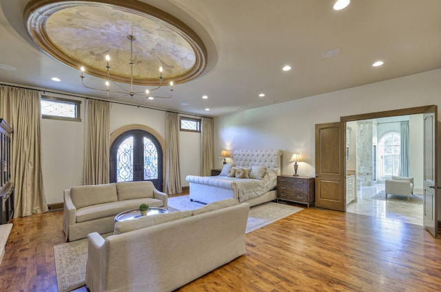 bedroom with light wood finished floors, multiple windows, a raised ceiling, and french doors