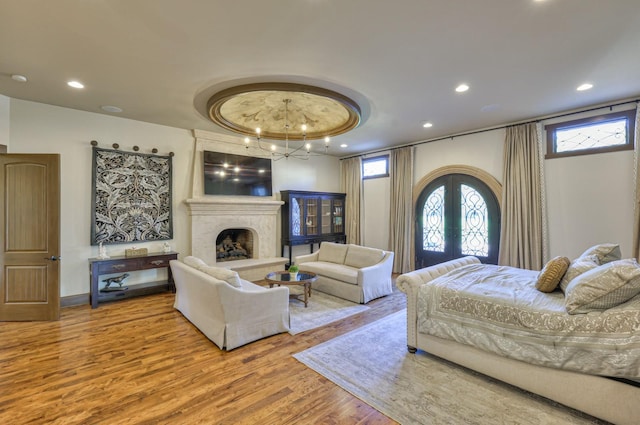 bedroom with arched walkways, wood finished floors, french doors, multiple windows, and a high end fireplace