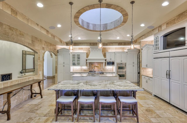 kitchen with stainless steel appliances, custom exhaust hood, a kitchen island, and stone tile floors