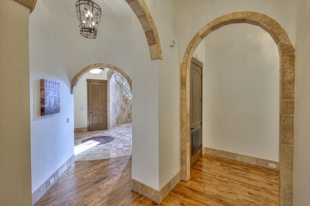 hall featuring a chandelier, arched walkways, baseboards, and wood finished floors