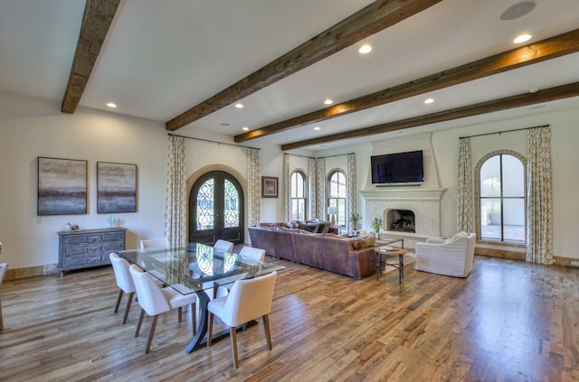 dining area featuring arched walkways, a fireplace with raised hearth, wood finished floors, baseboards, and french doors