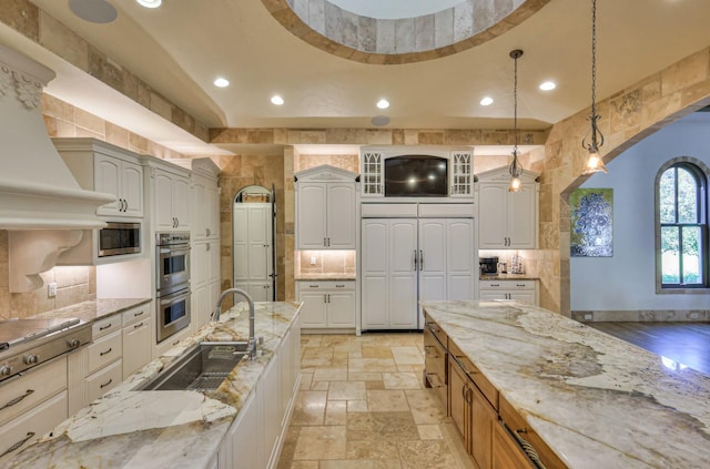 kitchen featuring appliances with stainless steel finishes, hanging light fixtures, light stone countertops, stone tile flooring, and a sink