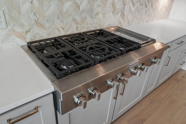 details featuring light wood finished floors, stainless steel gas stovetop, light countertops, and decorative backsplash