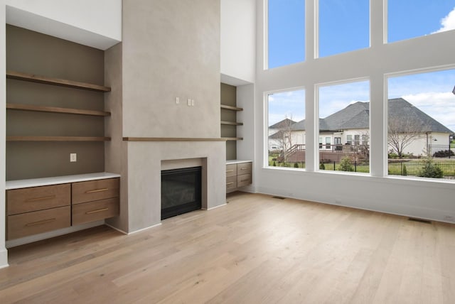 unfurnished living room with a towering ceiling, light wood-type flooring, and built in shelves