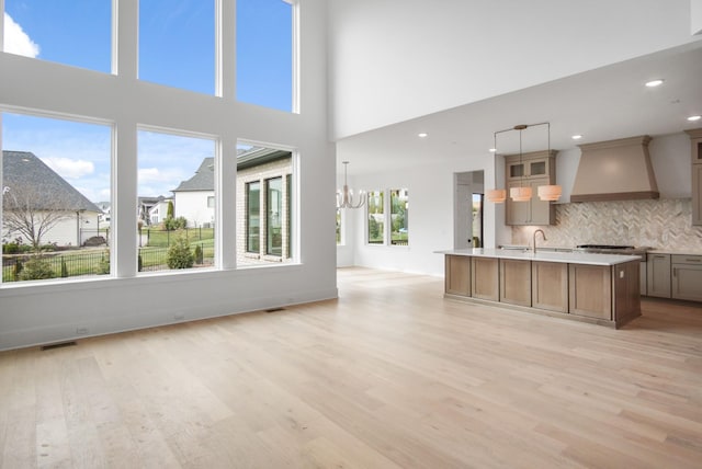 unfurnished living room with an inviting chandelier, sink, and light hardwood / wood-style flooring