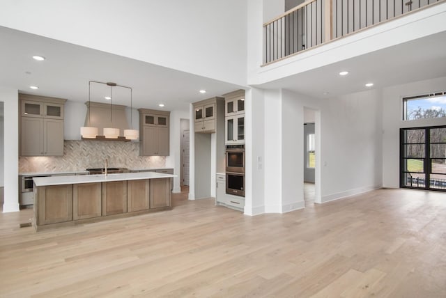 kitchen with glass insert cabinets, light countertops, a center island with sink, and hanging light fixtures