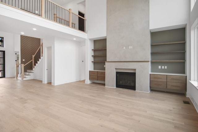 unfurnished living room featuring stairway, light wood-style flooring, built in shelves, and visible vents