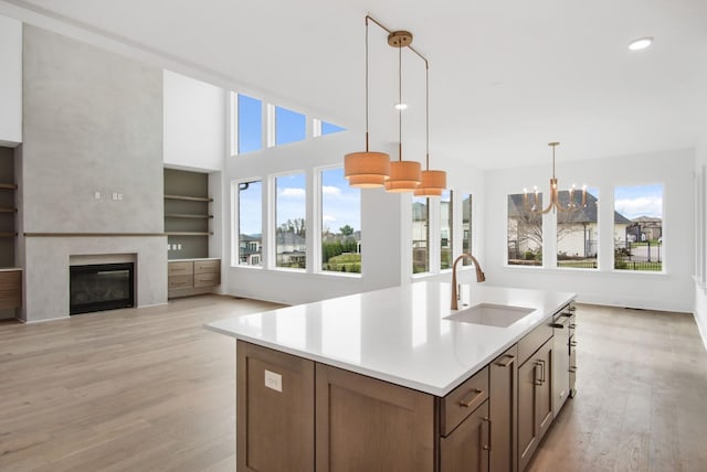 kitchen featuring built in features, an island with sink, sink, hanging light fixtures, and light hardwood / wood-style flooring