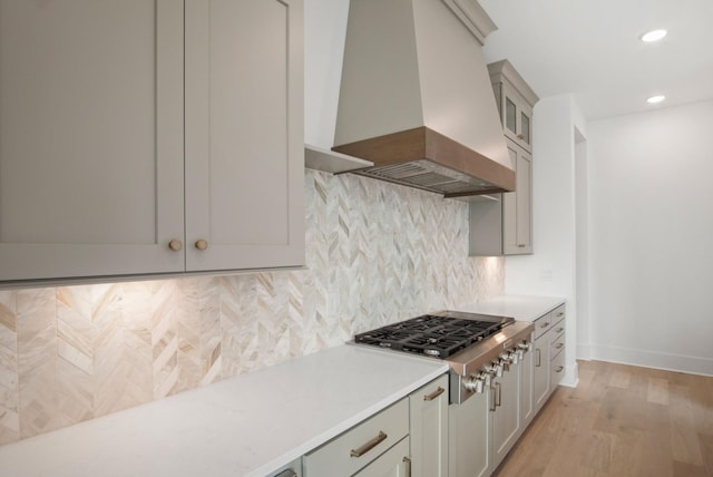 kitchen featuring stainless steel gas cooktop, light wood-type flooring, gray cabinets, custom range hood, and backsplash