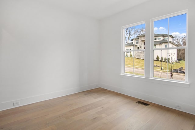 empty room featuring light wood-style flooring, visible vents, and baseboards