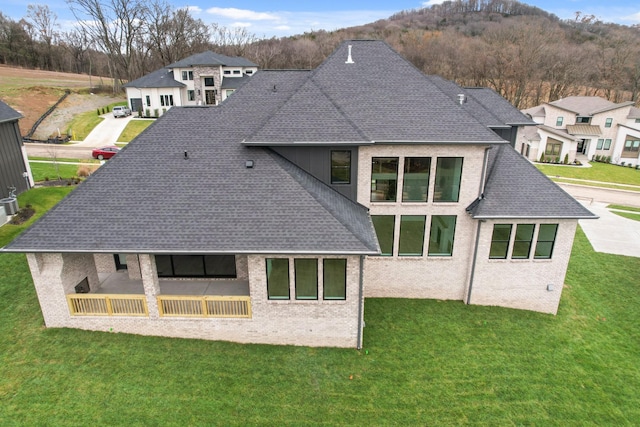 rear view of house featuring a shingled roof, a lawn, and brick siding