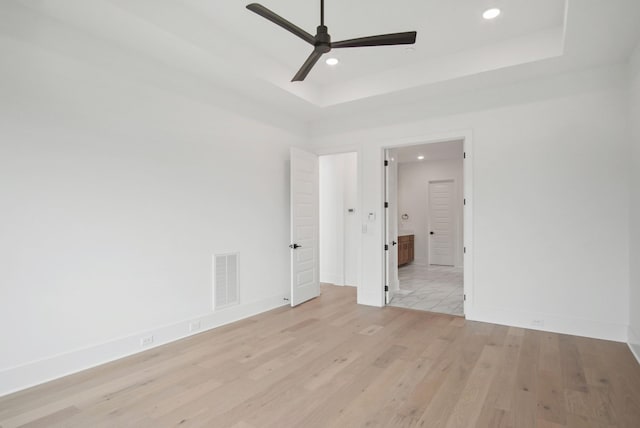 empty room with a raised ceiling, ceiling fan, and light hardwood / wood-style floors