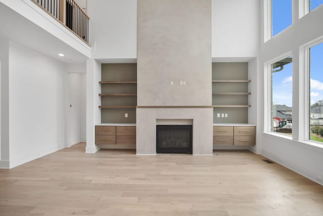6051 Lookaway Cir, Franklin, TN 37067 - unfurnished living room featuring a high ceiling, light wood-type flooring, a glass covered fireplace, and built in features