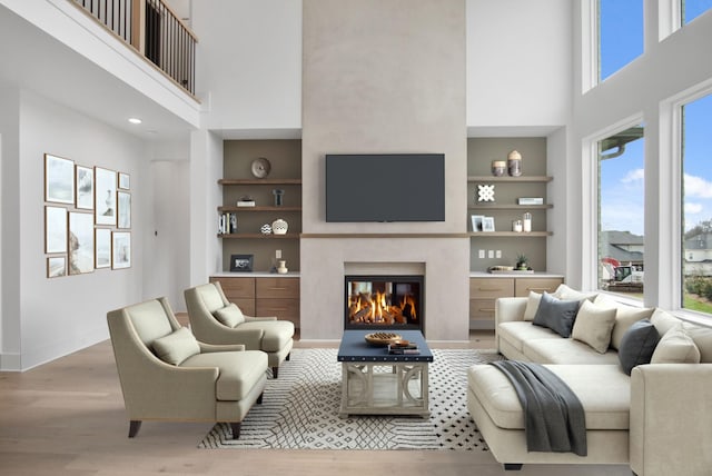 living room with built in shelves, plenty of natural light, a premium fireplace, and light hardwood / wood-style floors