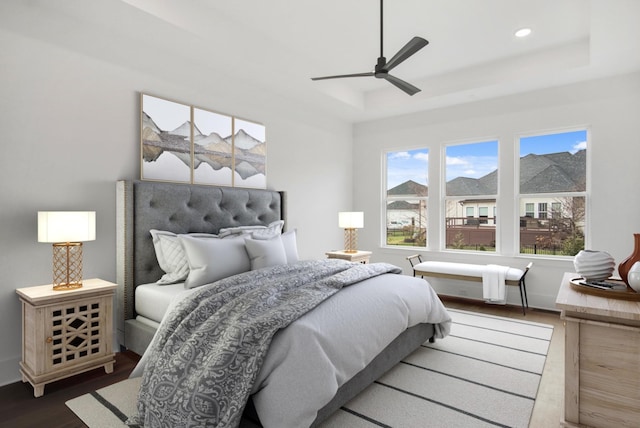 bedroom with hardwood / wood-style flooring, ceiling fan, and a raised ceiling