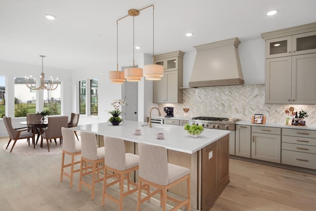 kitchen featuring decorative light fixtures, stainless steel gas stovetop, an island with sink, sink, and custom exhaust hood