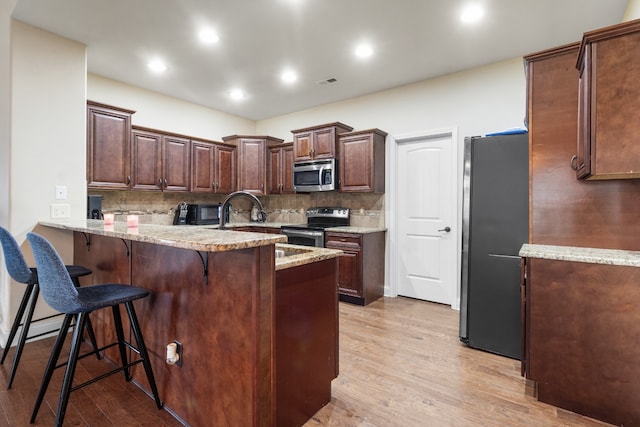 kitchen featuring light wood-type flooring, kitchen peninsula, backsplash, stainless steel appliances, and a kitchen breakfast bar