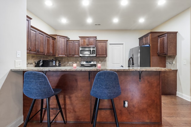 kitchen with light hardwood / wood-style flooring, tasteful backsplash, light stone counters, and stainless steel appliances