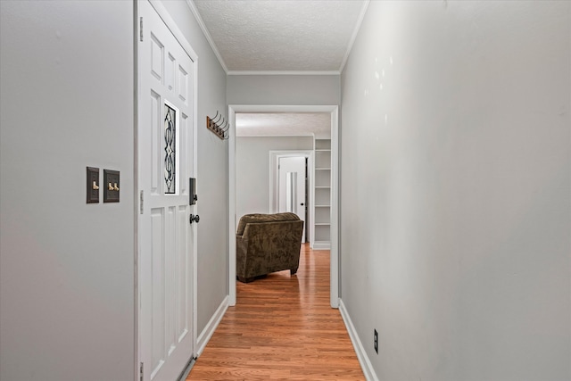 hallway featuring a textured ceiling, ornamental molding, and light wood-type flooring