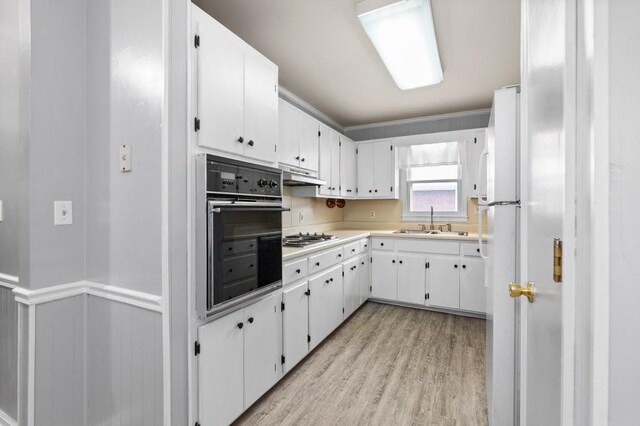 kitchen with white cabinets, stainless steel gas stovetop, oven, sink, and light hardwood / wood-style floors