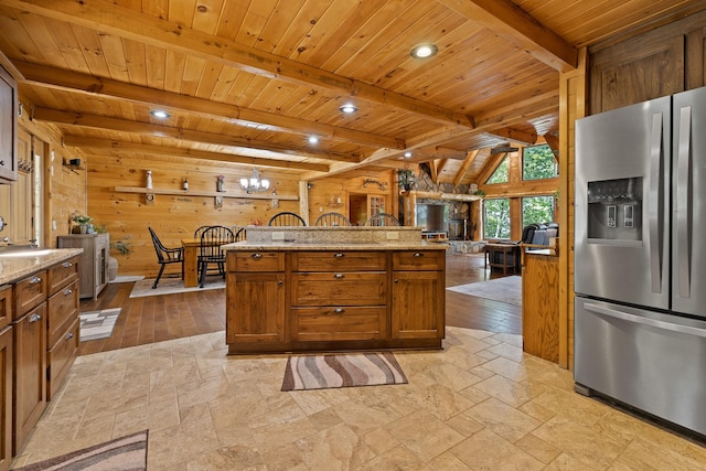 kitchen featuring wood ceiling, an inviting chandelier, light stone counters, wood walls, and stainless steel fridge