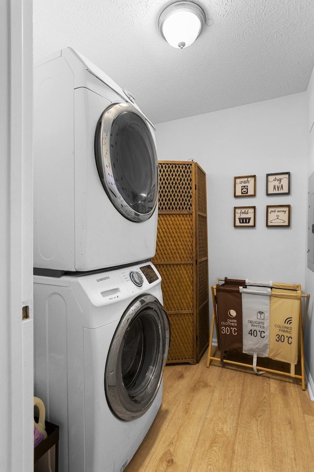 laundry room featuring stacked washer / drying machine, light wood-type flooring, and a textured ceiling