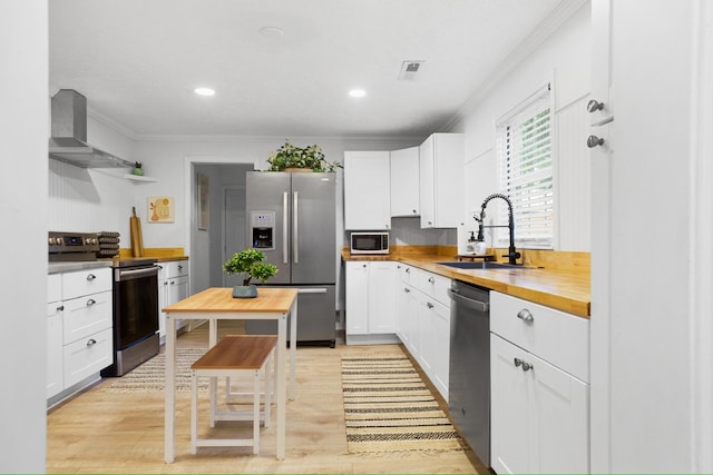 kitchen with white cabinetry, butcher block counters, stainless steel appliances, and wall chimney range hood