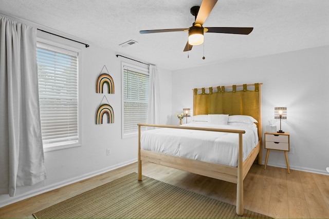 bedroom with ceiling fan, wood-type flooring, and a textured ceiling