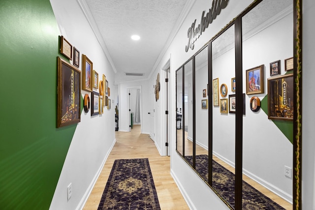 corridor with light hardwood / wood-style floors, a textured ceiling, and ornamental molding