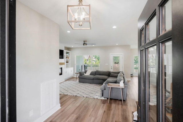 living room with ceiling fan with notable chandelier and light hardwood / wood-style flooring